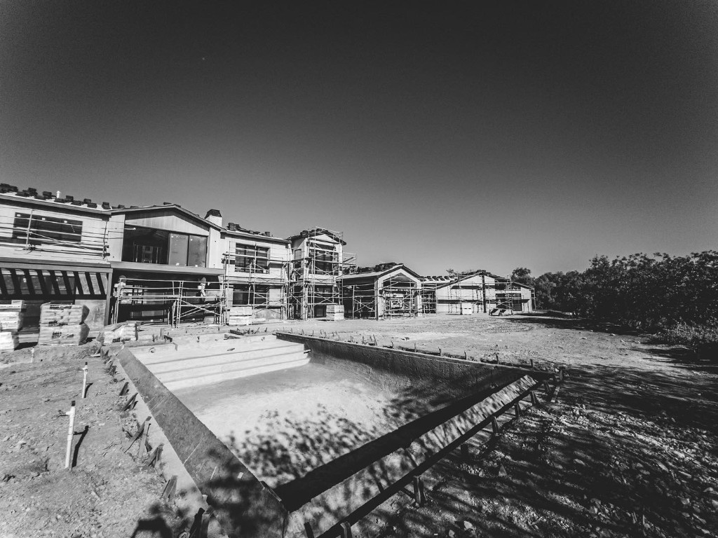 Custom home under construction with scaffolding and pool excavation